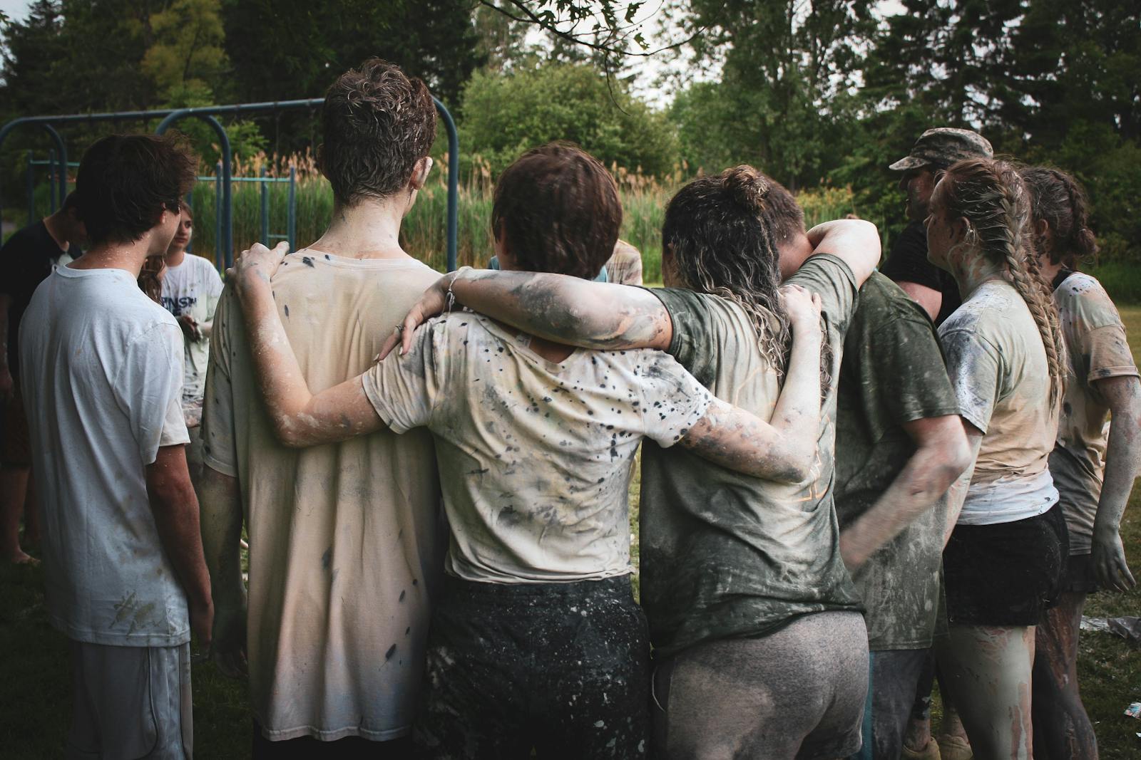 Group of teenagers bonding in a muddy team-building exercise outdoors.